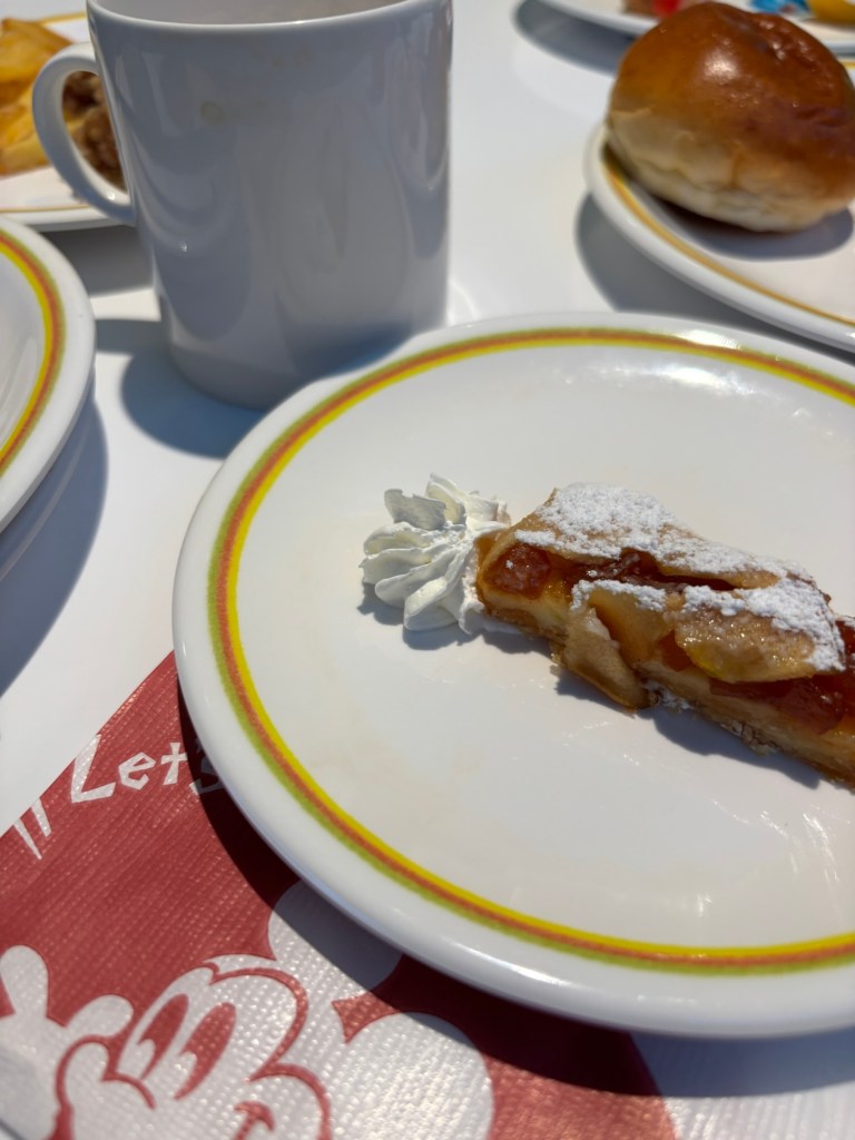 皿の上のアップルパイとホイップクリーム、背景には白いマグカップと他の料理があるテーブル