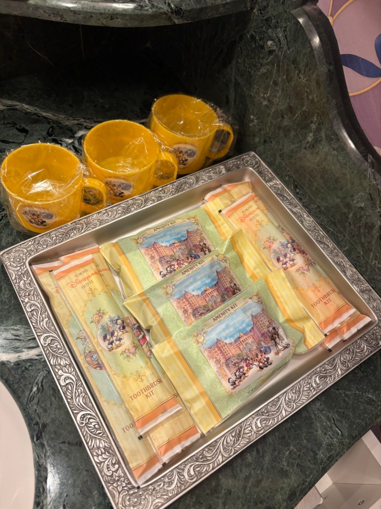 黄色のカップとアメニティキットが置かれたトレーの画像。トレーには歯ブラシキットやその他のアメニティが含まれている。