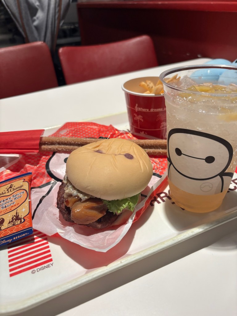ディズニーレストランでの食事のプレートに乗ったハンバーガー、ポテトと飲み物。ハンバーガーはレタスとソースが入っている。
